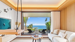 A modern living room with a large window offering a view of the ocean and palm trees. - Lil' Home (St. Barthelemy)
