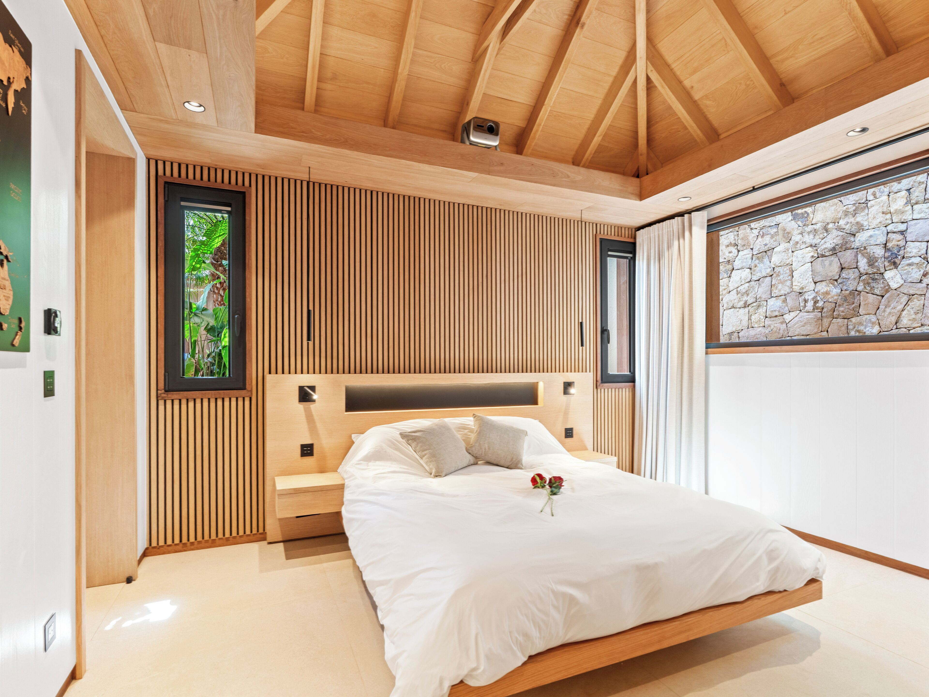 Un dormitorio moderno con techo de madera, pared de piedra y cama con ropa blanca.