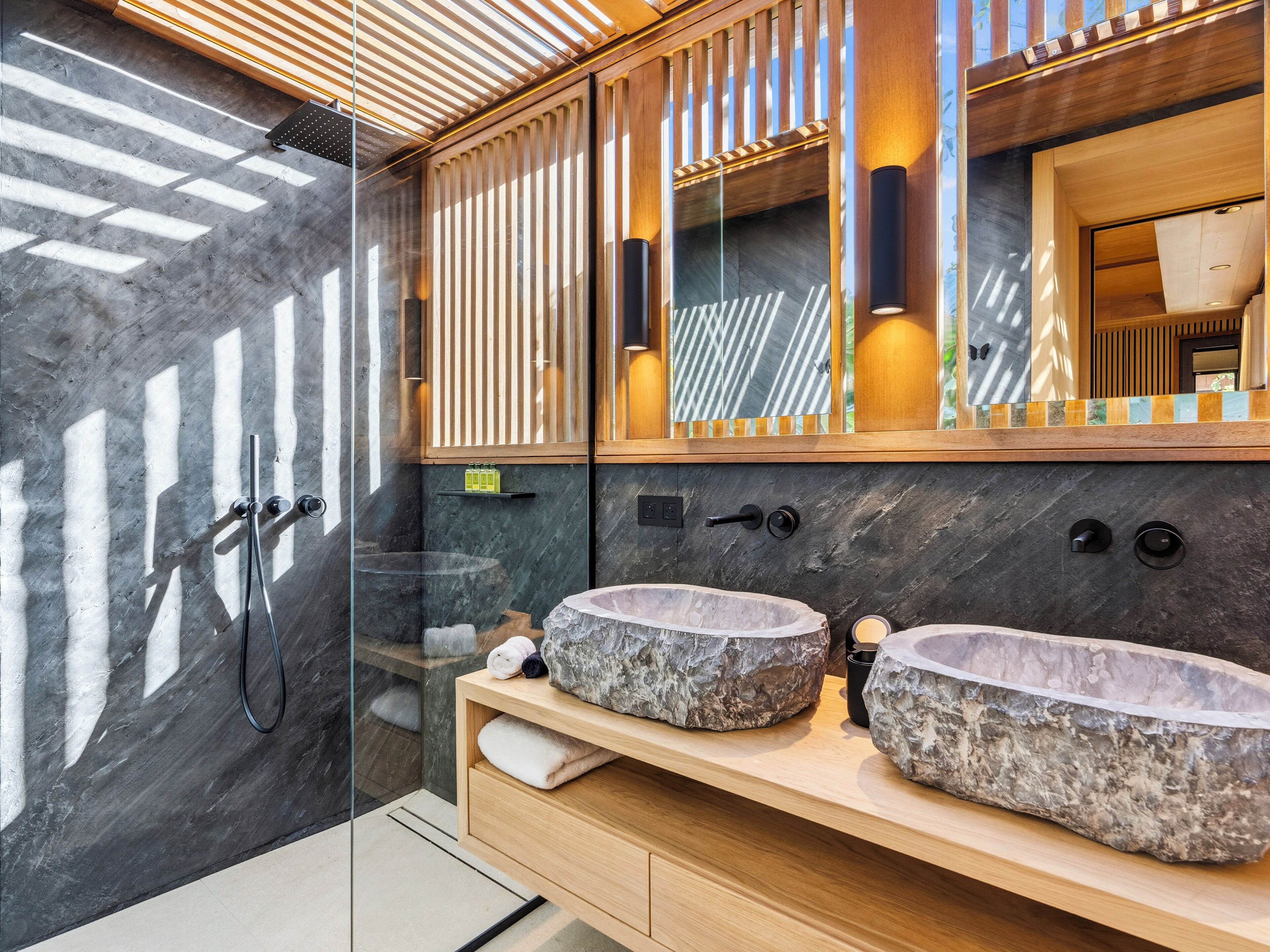 Une salle de bain moderne avec deux vasques en pierre, une douche en verre et un meuble-lavabo en bois.