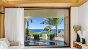A modern living room with a large glass door leading to a balcony with a view of the ocean. - Lil' Home (St. Barthelemy)