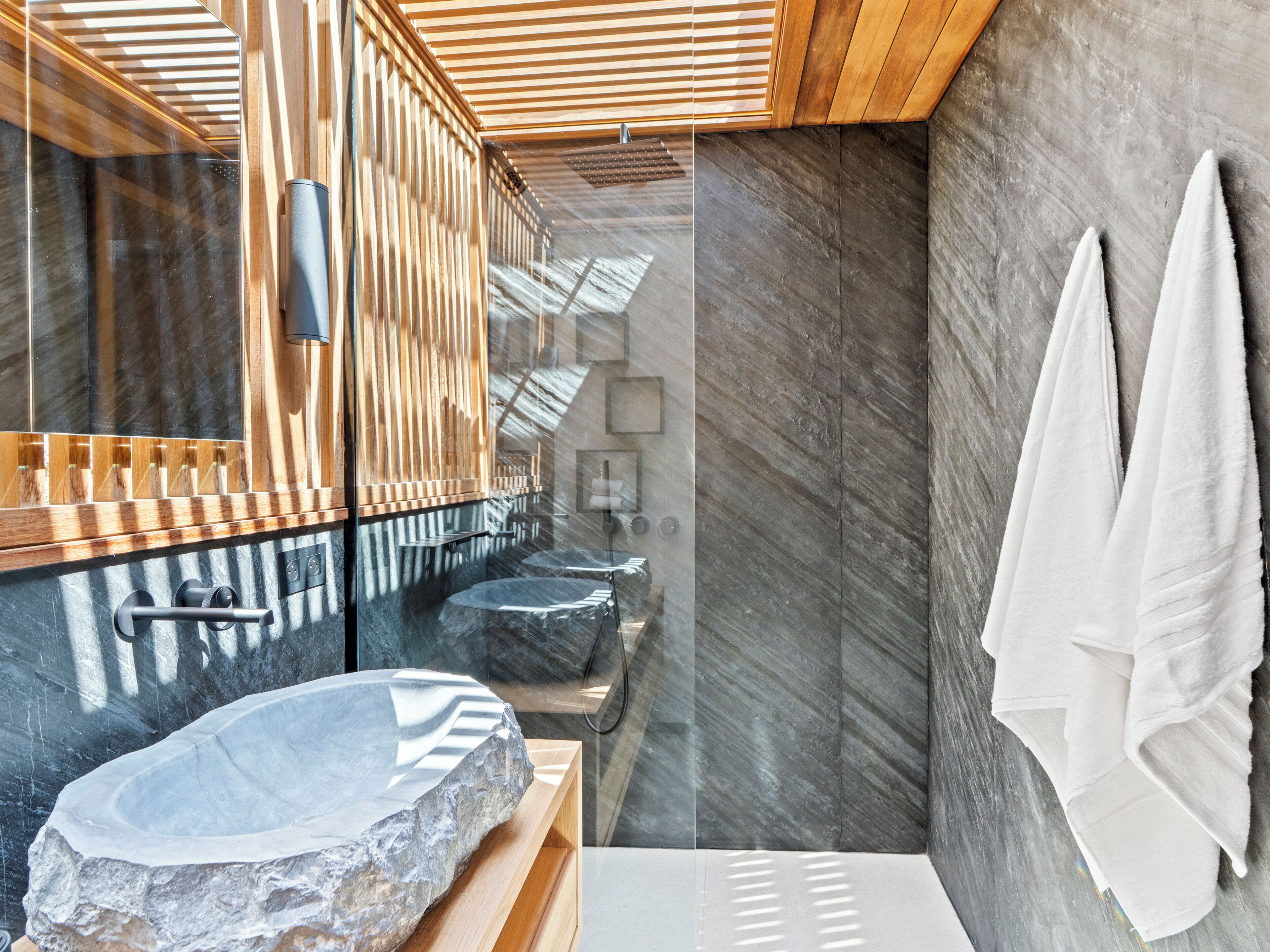 Un baño moderno con un lavabo de piedra grande, paneles de madera y una mampara de cristal.