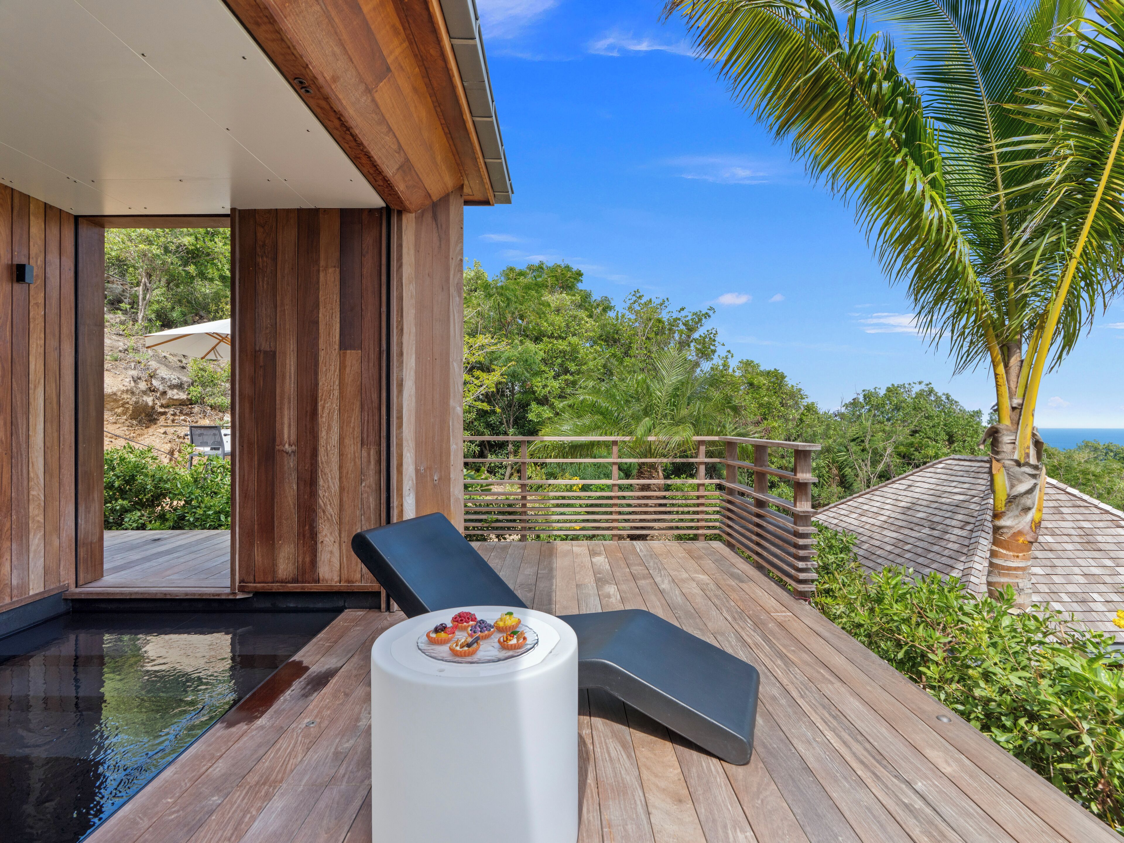 A wooden deck with a pool, a lounge chair, and a table with fruit.