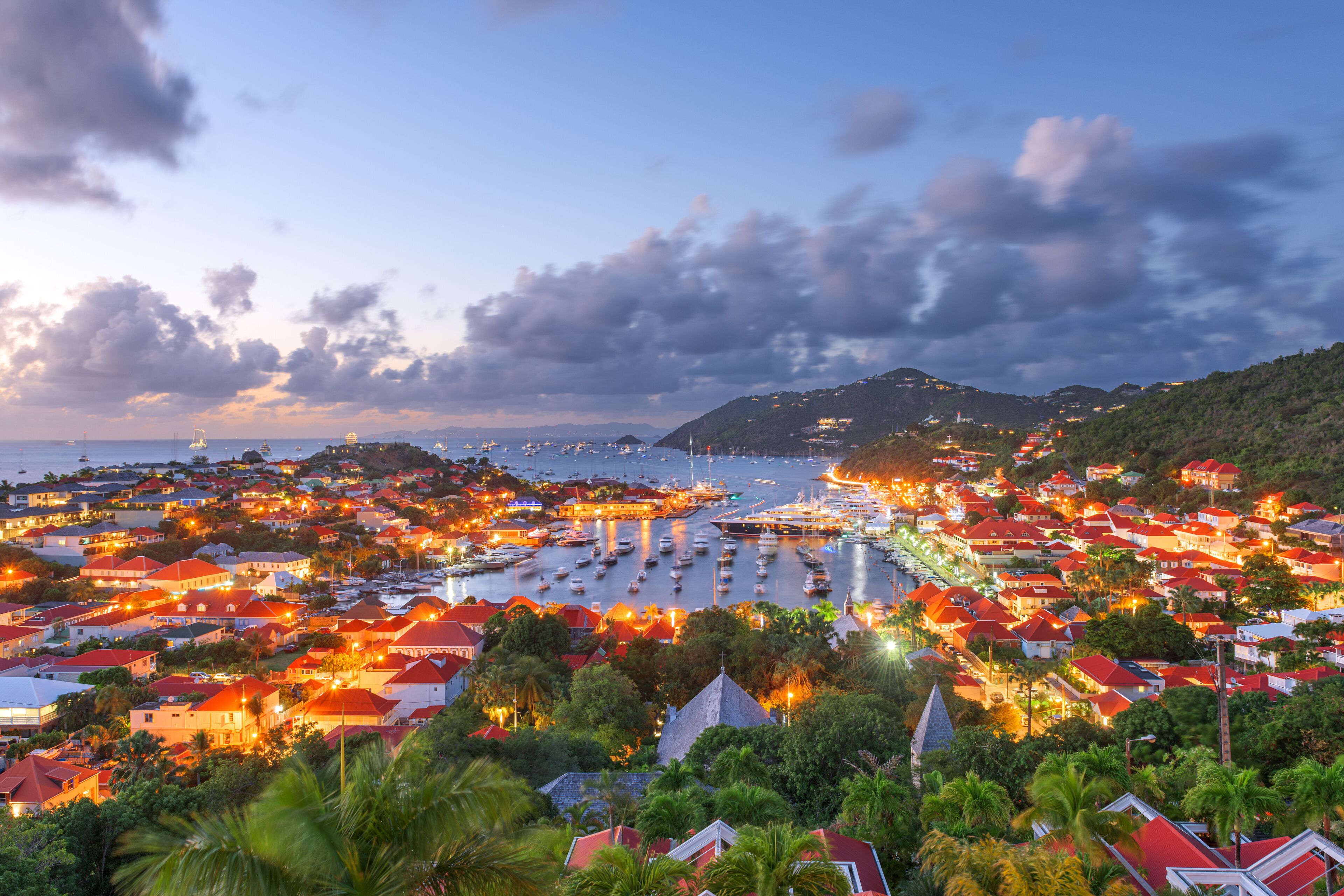 A coastal town with numerous buildings, a marina with boats, and a hilly backdrop.