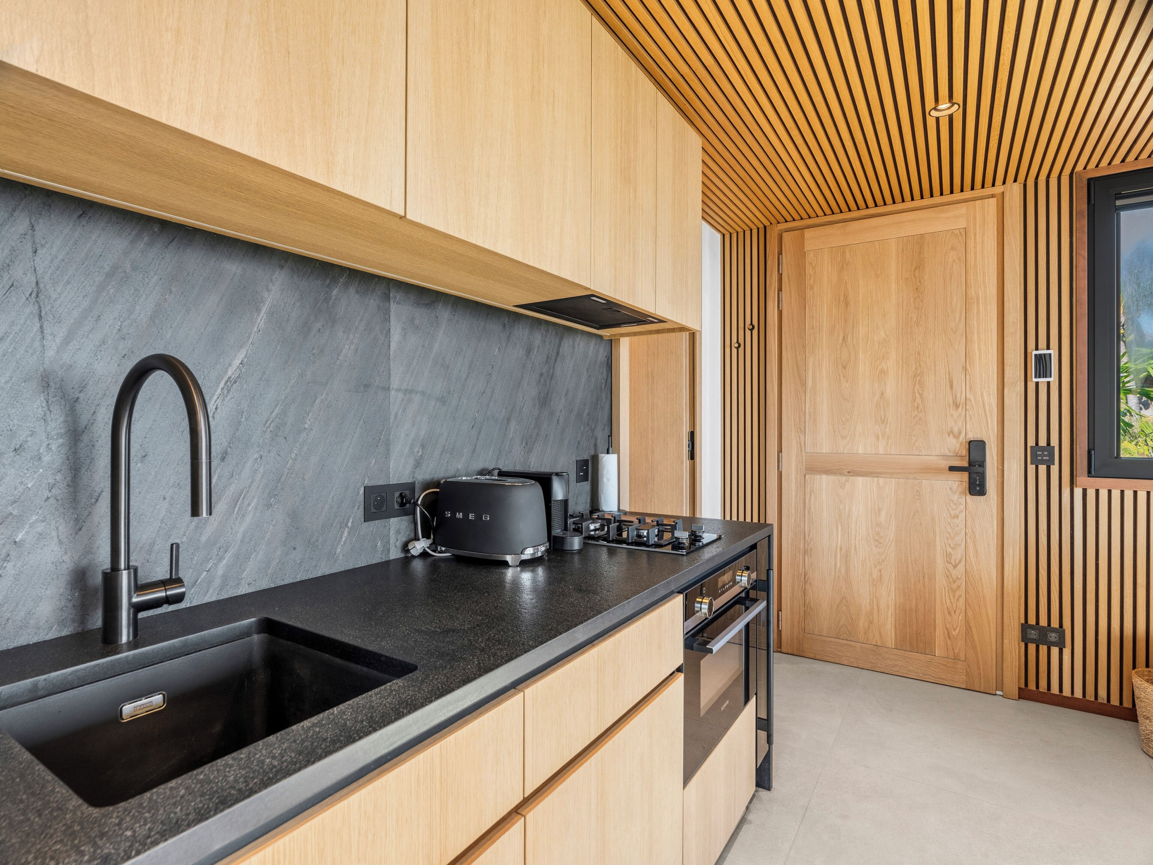 Una cocina moderna con un lavamanos negro, un tostador y armarios de madera.
