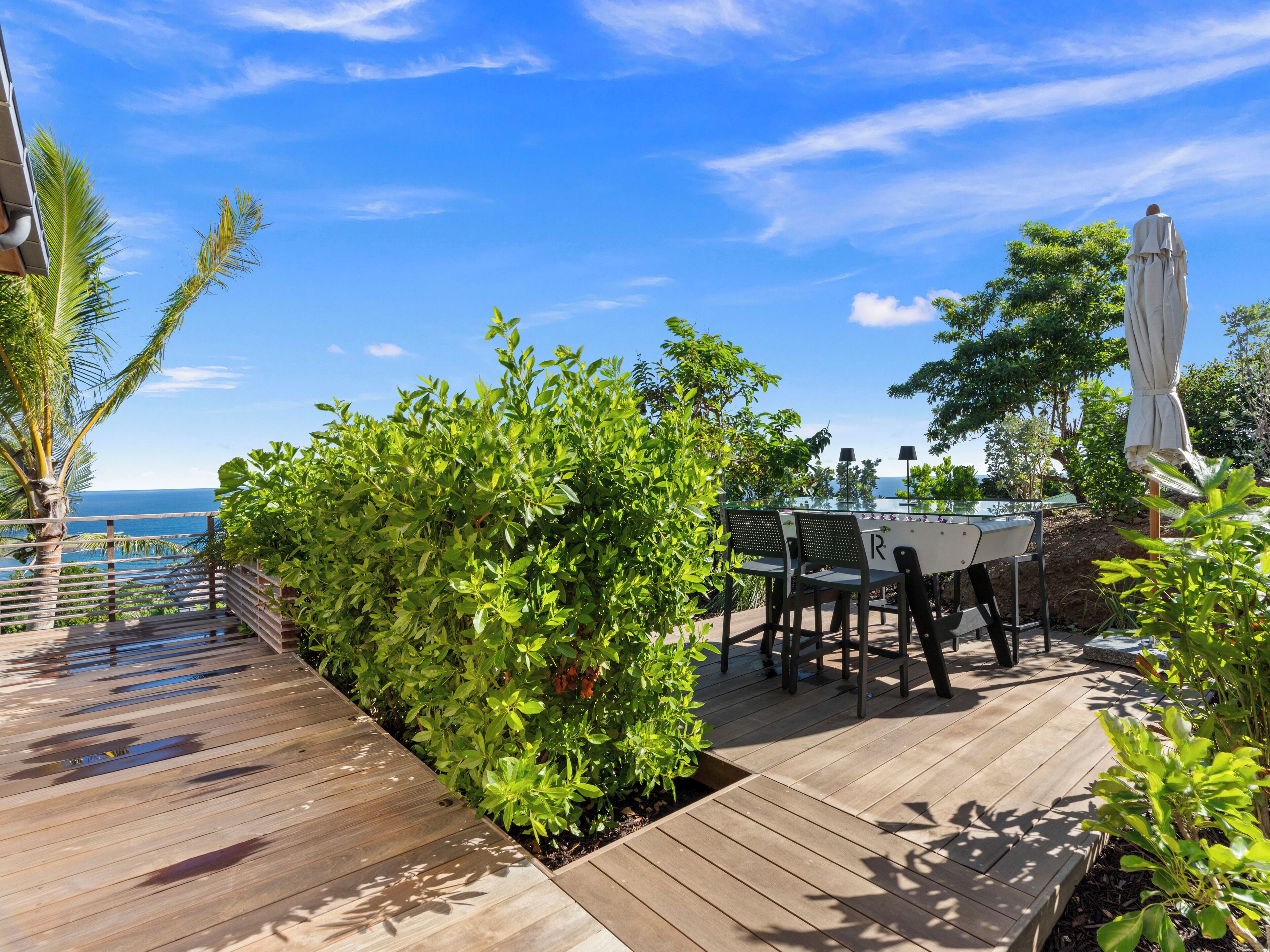 A wooden deck with a table and chairs, surrounded by lush greenery and overlooking a body of water.