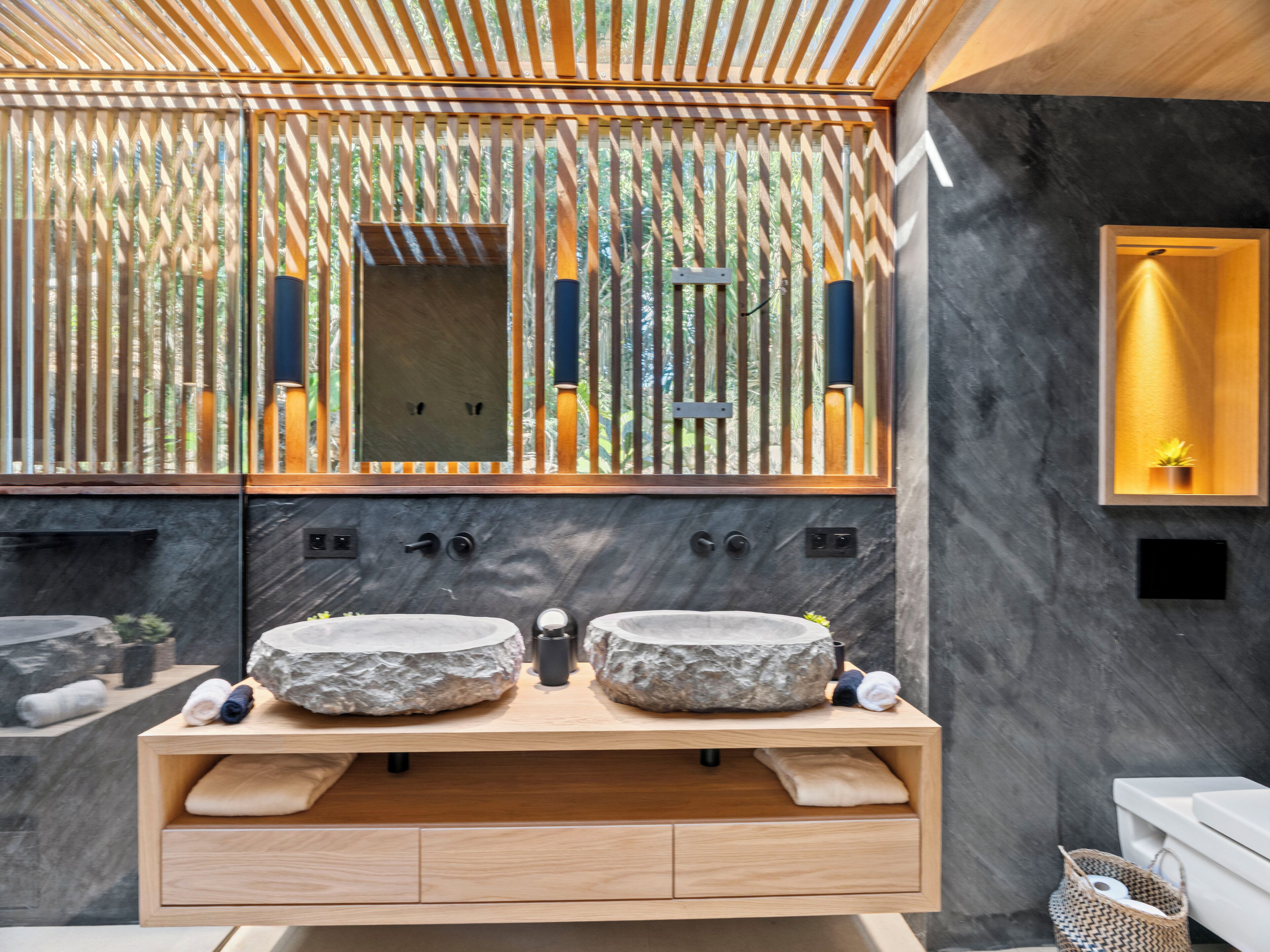 Un bagno moderno con due lavabi in pietra, un mobile contenitore in legno e uno specchio grande.