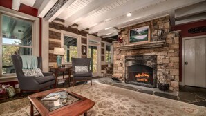 Un salon avec une cheminée en pierre, deux fauteuils, une table basse et une grande fenêtre.