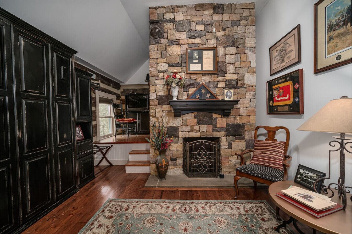 A cozy living room with a stone fireplace, dark wooden cabinets, a patterned rug, and a comfortable chair.
