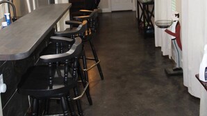 A kitchen with a long counter, black bar stools, stainless steel appliances, pendant lights, and a door with a mirror.