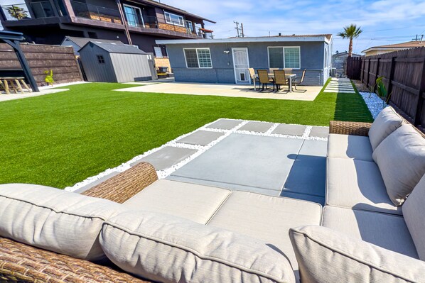 Un patio trasero con mobiliario exterior y una casa al fondo.