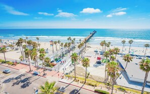 A coastal cityscape with a prominent pier extending into the ocean, palm trees lining the streets, and a clear blue sky. - OceanSide, CA Retreat, 5 Min Drive to Beach & Pier, King Bed, A/C, Big Backyard (Oceanside)