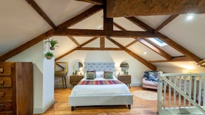 Une chambre avec un grand lit, des poutres apparentes en bois au plafond, une commode, un bureau et un petit balcon.