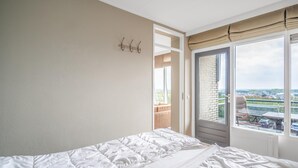 Ein Schlafzimmer mit einem Bett, einer Tür, die auf einen Balkon führt, und Blick ins Freie.