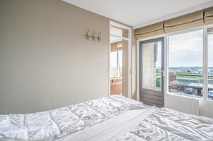 A bedroom with a bed, a door leading to a balcony, and a view of the outside.