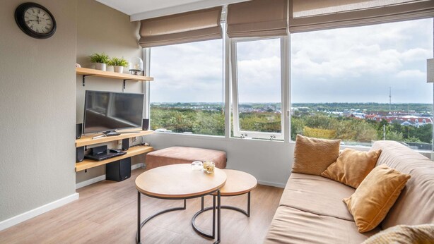 Ein modernes Wohnzimmer mit großem Fenster, Flachbildfernseher, Sofa und kleinem runden Tisch.