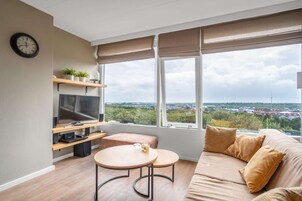 Ein modernes Wohnzimmer mit großem Fenster, Flachbildfernseher, Sofa und kleinem runden Tisch.