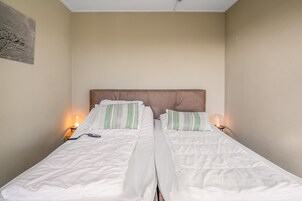 Ein Doppelbett mit weißer Bettwäsche, grün gestreiften Kissen, einem Holzkopfende und Nachttischlampen.