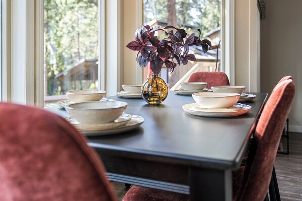 A dining table set with bowls, plates, and a vase with a plant. - Cozy Doe Cabin: Family Friendly, 5 Min Walk to Village SHARC passes + Hot Tub (Sunriver)