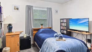 Quarto com cama, escrivaninha, estante, televisão e ventilador de teto.