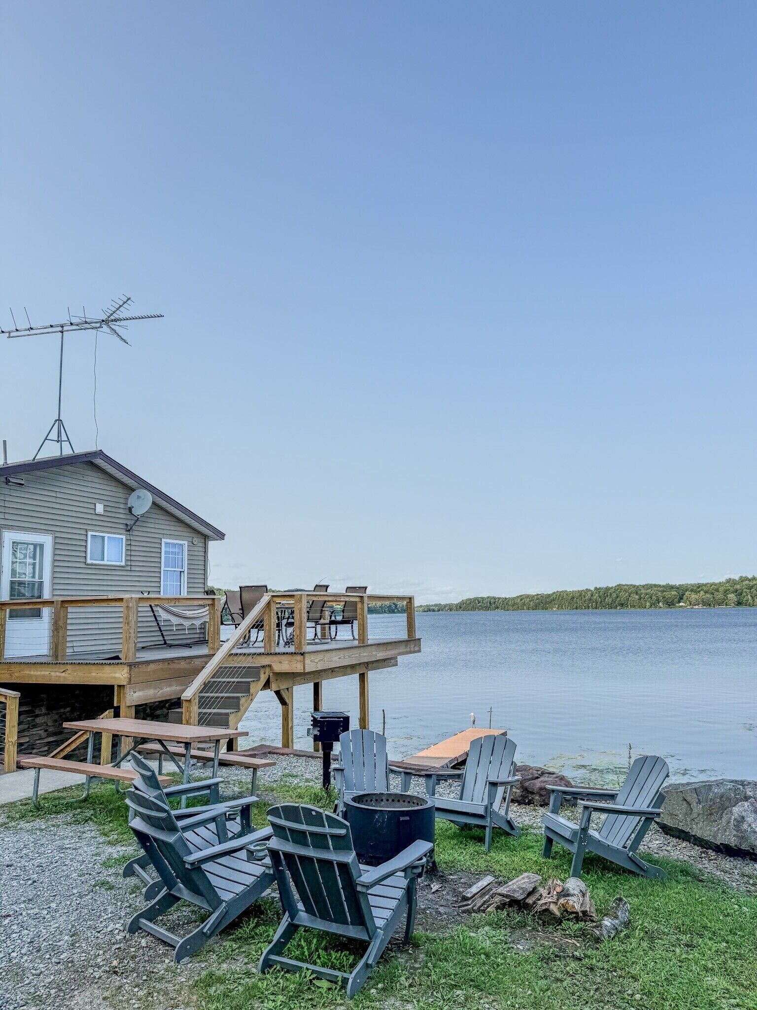 Una cabaña junto al lago con terraza, mobiliario exterior y un brasero.