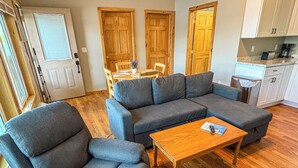 A living room with a sectional sofa, a single armchair, a wooden coffee table, and a dining area with a table and chairs.