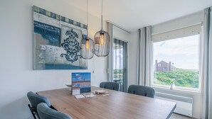 Un espace de salle à manger moderne avec une table en bois, des chaises à revêtement gris et des luminaires suspendus.