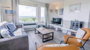 Un salon moderne comprenant un canapé, un fauteuil et une table basse, ainsi qu’un téléviseur à écran plat et une cheminée.