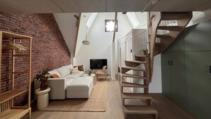 A loft-style living space with exposed brick, a staircase, and a large TV.