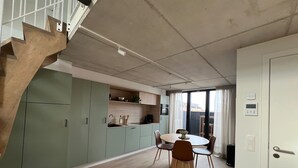 Una cucina moderna con mobili verdi, un'area pranzo con tavolo e sedie rotonde, e una scala in legno dal design particolare.