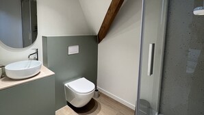 A modern bathroom with a round mirror, a white sink, and a toilet.