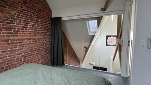 Una camera da letto con parete in mattoni, un letto con copriletto fantasia, una finestra con tende e vista su una scala.