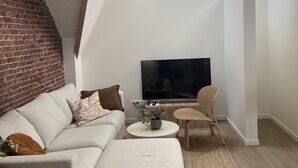 Un soggiorno moderno con parete in mattoni, televisore a schermo piatto, divano, tavolino e una poltrona.