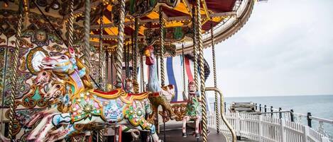 A carousel with ornate horses and a flag, located on a pier with a view of the sea.