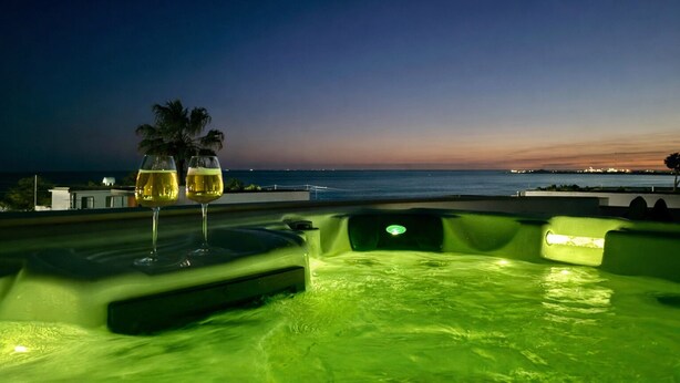 A rooftop pool with two glasses of wine, a palm tree, and a view of the ocean at dusk. - Vista Mare House | Private Spa Terrace • Sea View • (Santa Maria del Focallo)