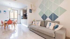 A modern living room with a sofa, dining table, and chairs. There is a kitchen area in the background. - Vista Mare House | Private Spa Terrace • Sea View • (Santa Maria del Focallo)