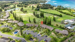 Oversigtsbillede af en golfbane med et klubhus, parkeringsområder og udsigt til havet.