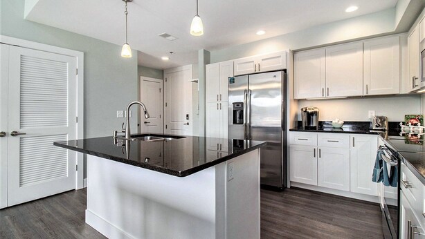 A modern kitchen with white cabinets, a stainless steel refrigerator, and a black countertop island. - 2 Bedroom Downtown Waterfront Condo (Manistee)