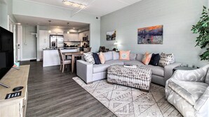 A modern living room with a grey sofa, ottoman, and a dining area with a table and chairs. - 2 Bedroom Downtown Waterfront Condo (Manistee)