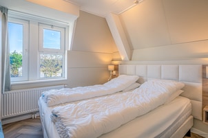 A bedroom with a large bed, a window with curtains, a wall-mounted lamp, and a radiator.