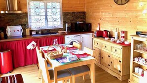 A cozy cabin interior with a wooden interior, a kitchen area with a stove, sink, and microwave, a dining table set for two, and a clock on the wall. - XIMISTA - BARDOS - Gîte (BARDOS)