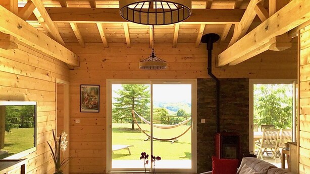 A cozy cabin interior with a wooden interior, a sofa, a fireplace, a hammock, and a view of the outdoors. - XIMISTA - BARDOS - Gîte (BARDOS)