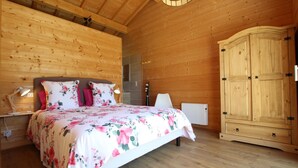 A wooden cabin bedroom with a bed, bedside lamps, a radiator, and a wardrobe. - XIMISTA - BARDOS - Gîte (BARDOS)