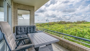 A balcony with a table and chairs, a view of greenery, and a brick wall. - 4 Person Apartment With sea View (De Koog)