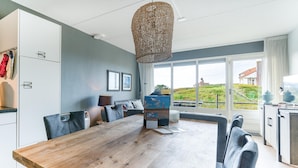A modern dining area with a wooden table, black chairs, and a woven light fixture. - 4 Person Apartment With sea View (De Koog)