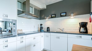 A modern kitchen with white cabinets, a built-in microwave, and a coffee maker. - 4 Person Apartment With sea View (De Koog)
