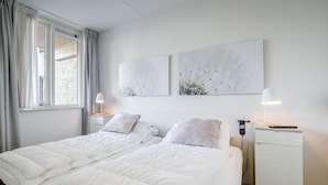 A double bed with white bedding, a bedside table with a lamp, and two wall-mounted artworks. - 4 Person Apartment With sea View (De Koog)