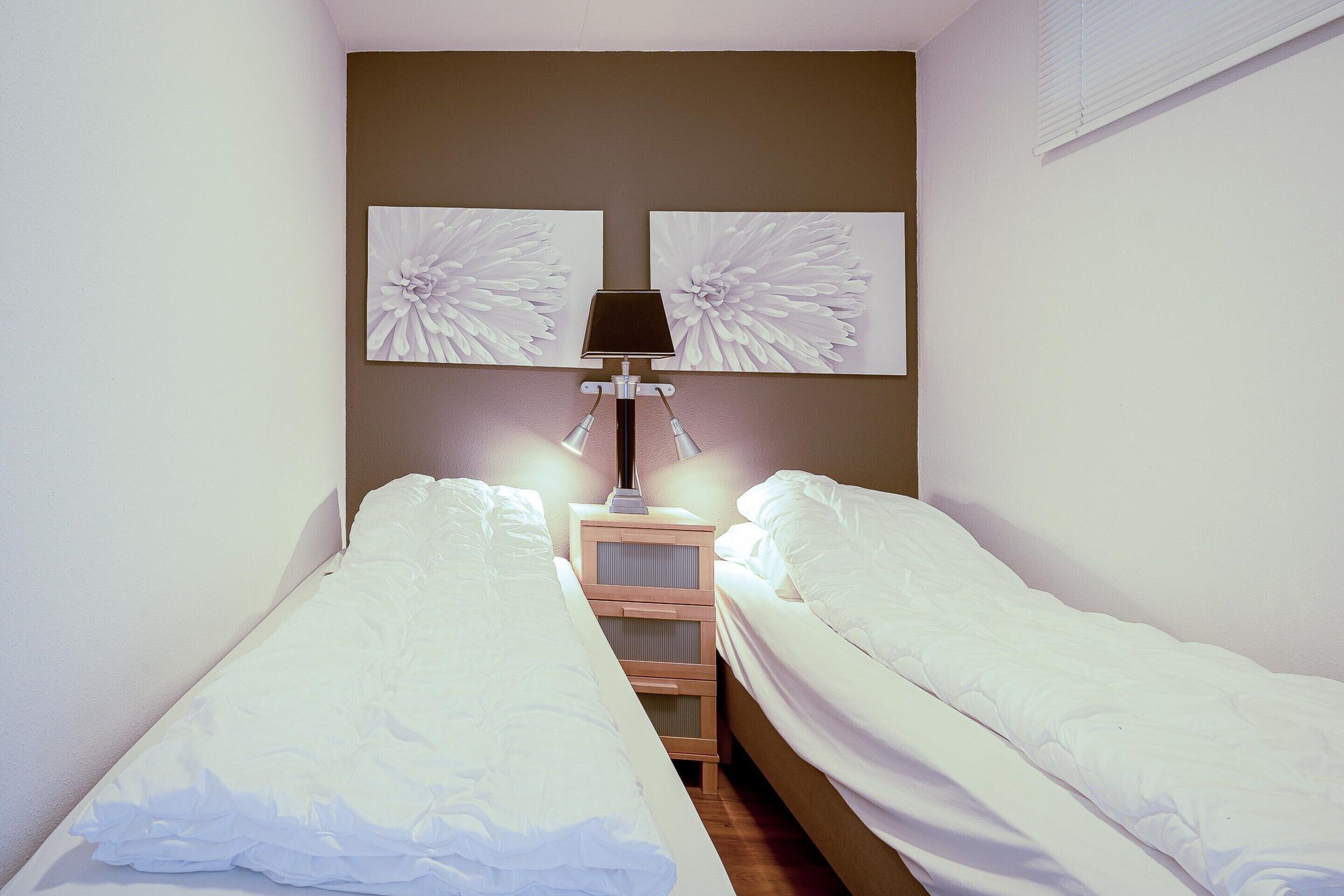 A bedroom with two single beds, a nightstand with a lamp, and two wall-mounted flower paintings.