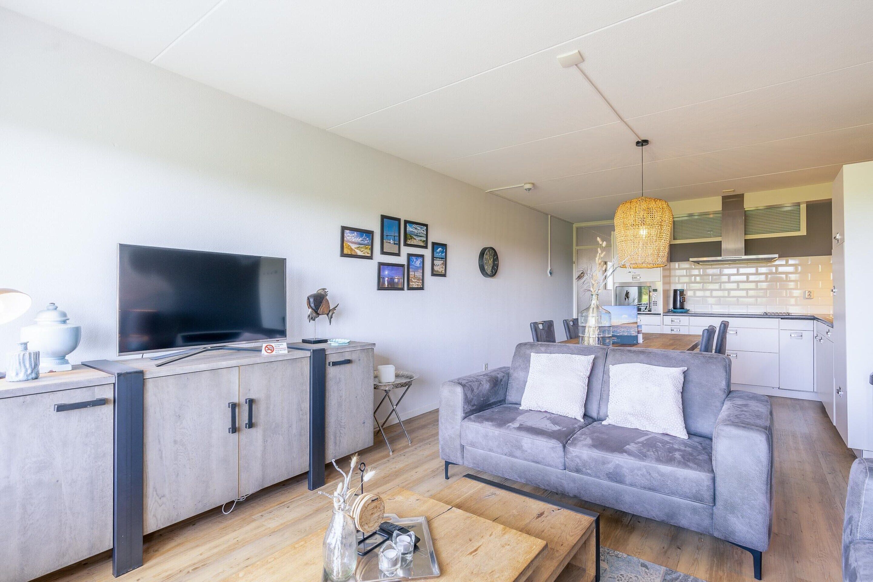Un salon moderne avec un canapé gris, une table basse en bois et un téléviseur à écran plat.