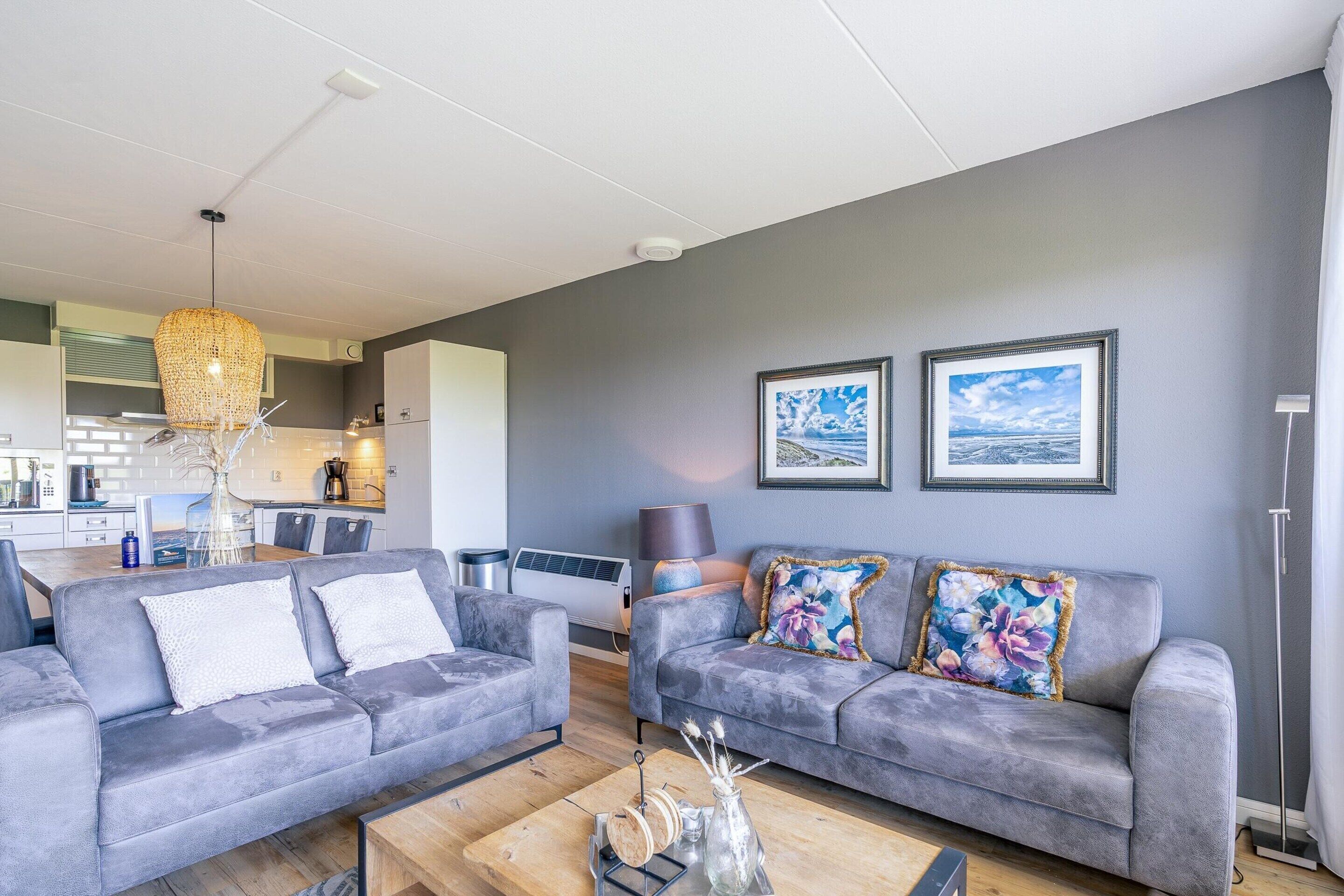 A modern living room with two grey sofas, a coffee table, and a dining area in the background.