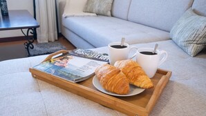En bakke med croissanter, to kopper kaffe og et magasin på en sofa.